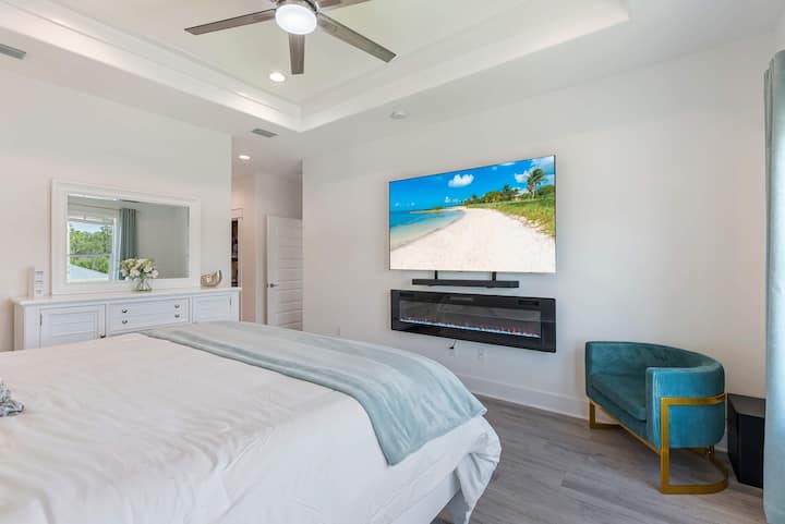 Dormitorio principal con cama tamaño king, televisor inteligente LED Samsung grande, barra de sonido y altavoces Samsung, y chimenea LED que cambia de color