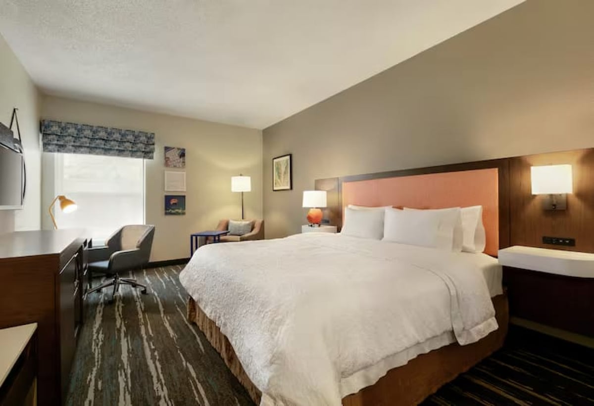 Manželská posteľ pri okne s písacím stolom a oranžovou stoličkou