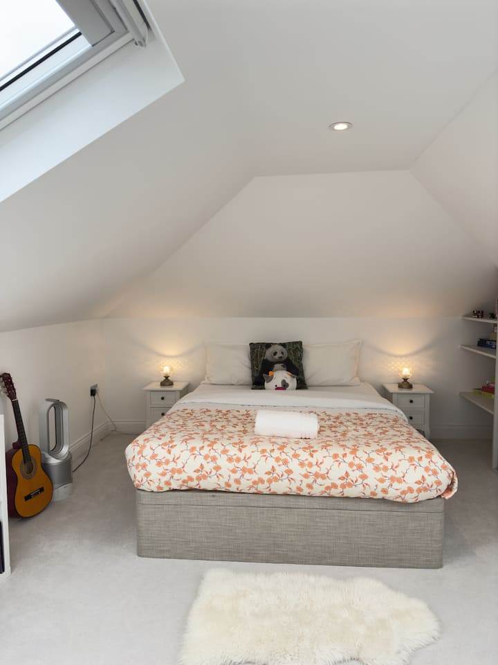 Encantador dormitorio tipo loft con techos inclinados y armarios empotrados. Acogedor y luminoso, es un refugio perfecto o una habitación divertida para los niños, con estanterías abiertas para almacenamiento y exhibición.