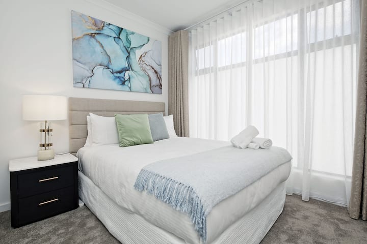 מרקמים רכים, אמנות בהשראת האוקיינוס ווילונות שקופים מהרצפה עד התקרה יוצרים אווירה רגועה בחדר השינה המואר הזה.