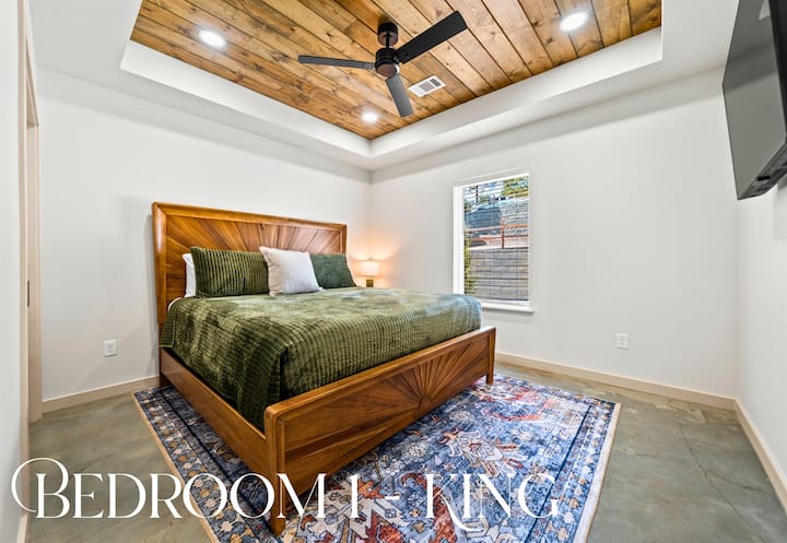 غرفة نوم كبيرة مع لمسات خشبية ومفروشات ناعمة ومروحة سقف لتوفير أقصى درجات الراحة.