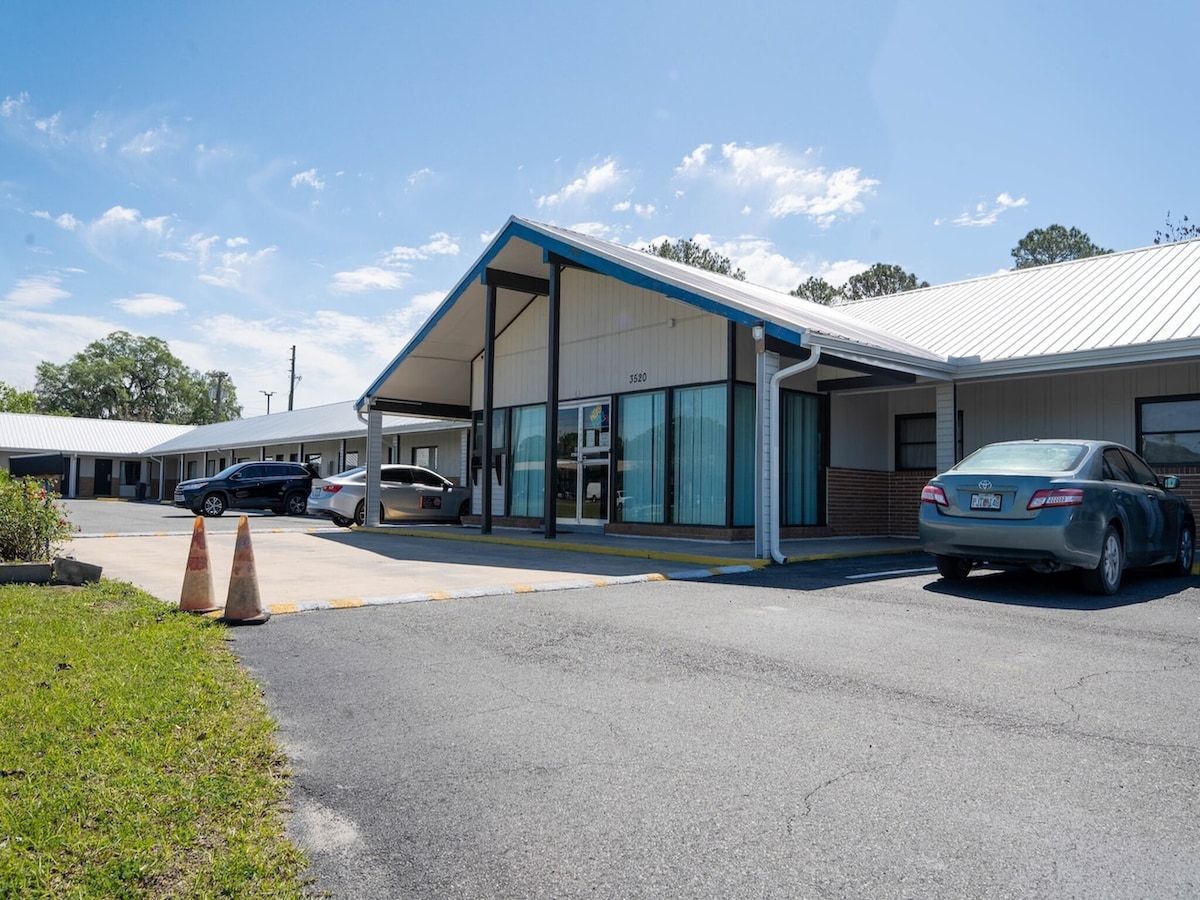 A single-story commercial building is presented, featuring a sloped roof with blue accents. Large glass windows allow visibility into the spacious interior. Parking spaces are available in front, with a well-maintained asphalt surface and grassy areas bordering the property.