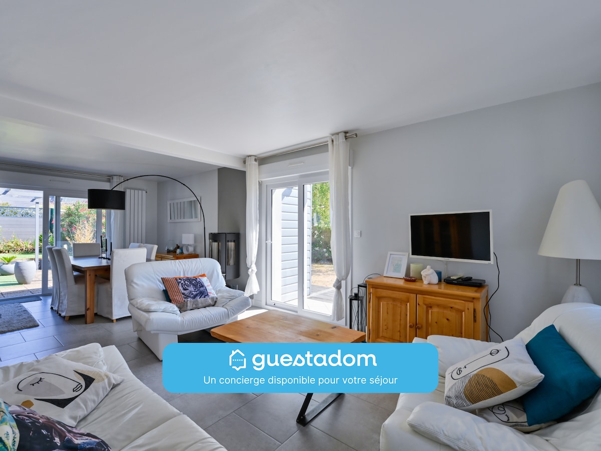 The living room features a comfortable seating arrangement with a sofa and armchairs. A television is positioned on a wooden cabinet, and large glass doors provide access to the terrace, allowing natural light to fill the space.