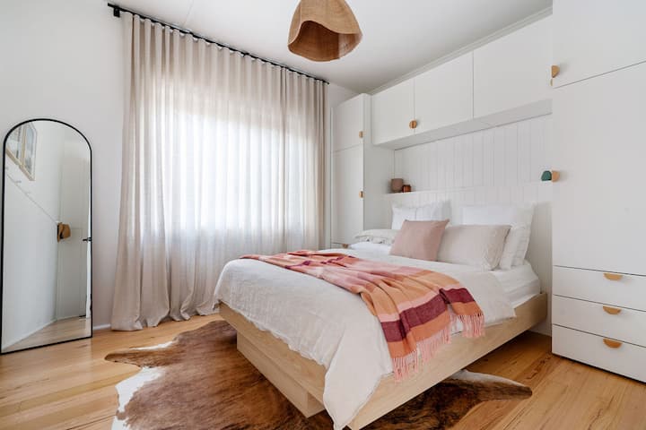 Chambre minimaliste ensoleillée avec lit flottant, meubles encastrés et draps confortables