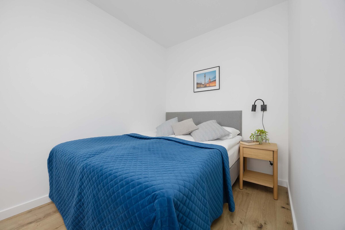 Útulná spálňa s tmavomodrou posteľou zaručuje pokojný spánok, zatiaľ čo neutrálna farebná paleta vytvára pokojnú a relaxačnú atmosféru.