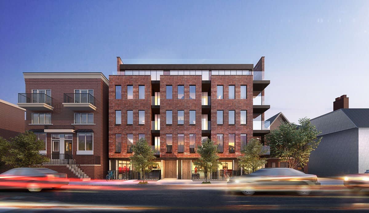 A contemporary four-story brick building is featured, showcasing a symmetrical design with large windows and balconies. The surrounding streetscape includes trees and parked bicycles, with modern vehicles passing by, capturing a bustling urban atmosphere during twilight.
