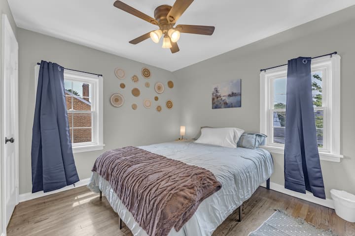 - חדר שינה עם מיטת קווין סייז ומצעים רכים וצוננים - אור טבעי משני חלונות עם וילונות כחולים - עיצוב קיר מוסיף קסם ואווירה נעימה  