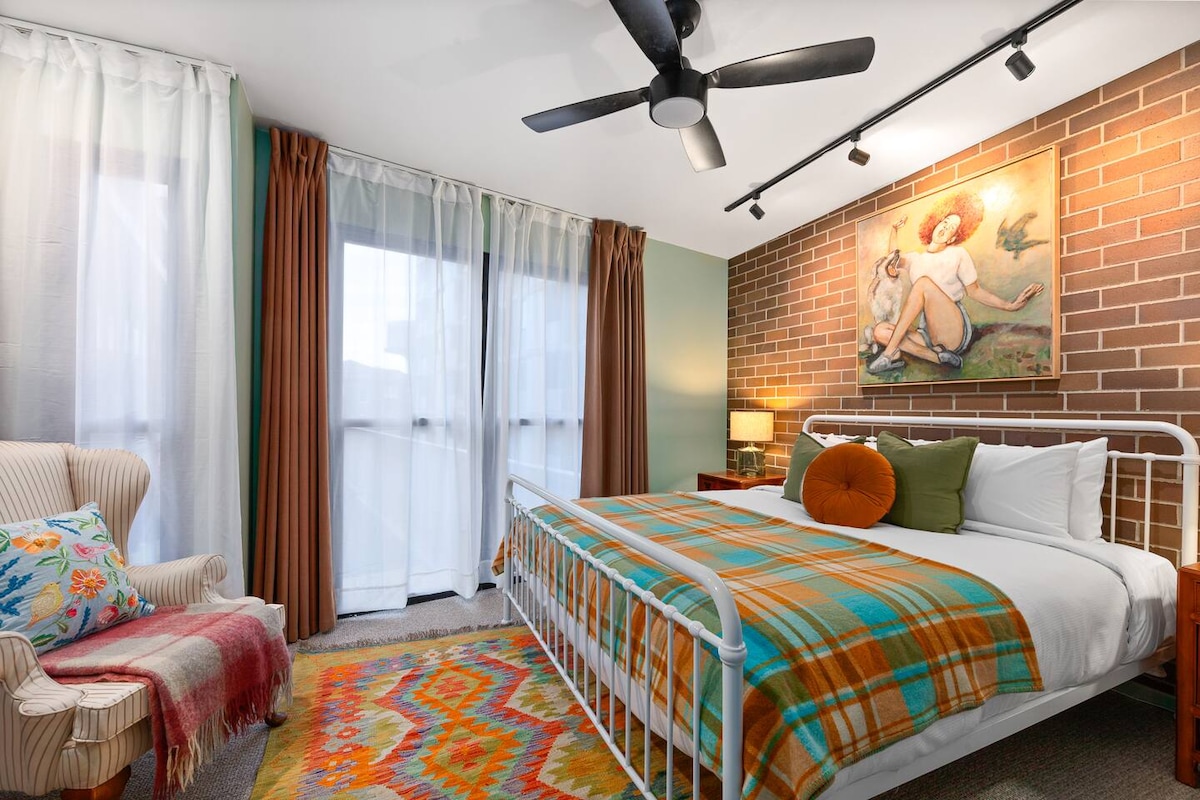 Utonite u veliki bračni krevet u prvoj spavaćoj sobi uokvirenoj odvažnim umjetničkim djelima i vidljivom ciglom, s udobnom foteljom, stropnim ventilatorom i promišljenim stilom koji stvara topao, miran prostor.
