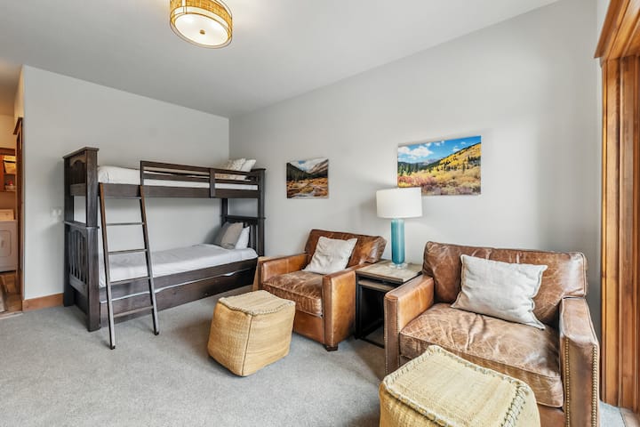 休息区：双层床、低层、附近有洗衣机/烘干机、两把带脚凳的扶手椅、衣柜、热水浴缸