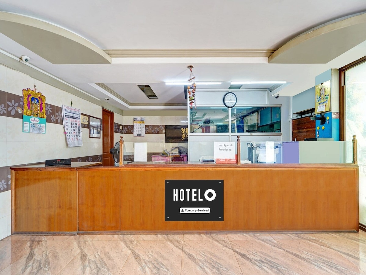 A modern reception area is visible, featuring a wooden front desk with the hotel logo prominently displayed. The space includes a wall clock and various informational posters. The flooring is adorned with polished marble, contributing to a clean and welcoming environment.