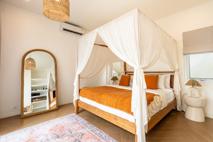 Acogedor dormitorio con cama con dosel y ropa de cama de color naranja brillante.