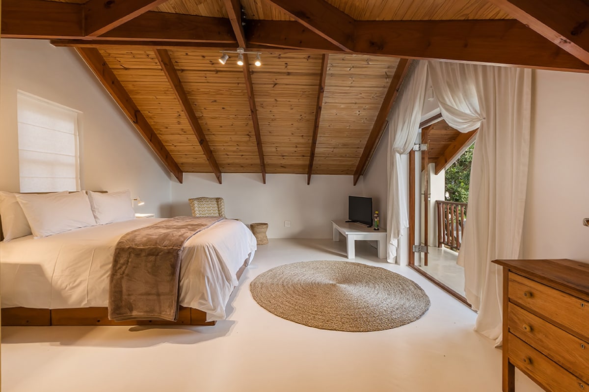 Een uitnodigende exotische oase waar natuurlijke houten balken samenkomen met een luchtige witte ruimte, waardoor een serene ontsnapping ontstaat die rust en eilandcharme fluistert.