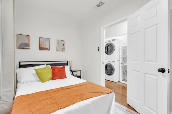 საძინებელი, რომელშიც არის ორადგილიანი საწოლი, ფანჯრის ბრმები, ფუფუნების საწოლ‑სახარში და ფერადი ხელოვნების ნამუშევრები.