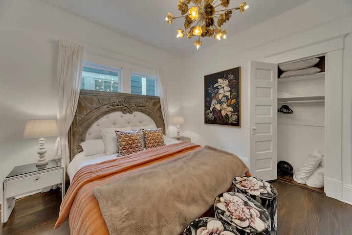 Elegante dormitorio principal con cama tamaño king, cabecera acolchada, detalles florales y un llamativo candelabro