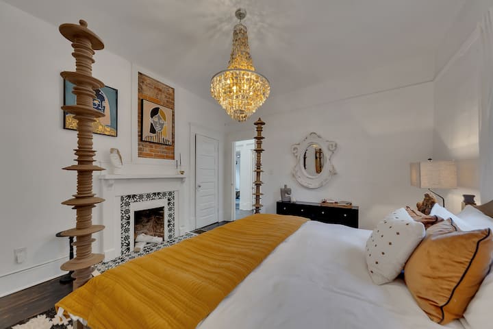 Elegante dormitorio con cama con dosel tallada, lámpara de araña de cristal y chimenea decorativa