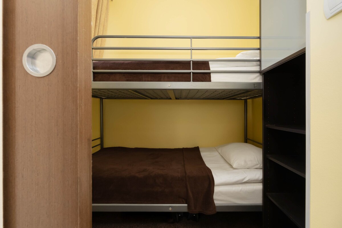 一个小睡眠角落，内置双层床，由木板和窗帘围成。 底部有一张单人床，配有床垫和枕头。