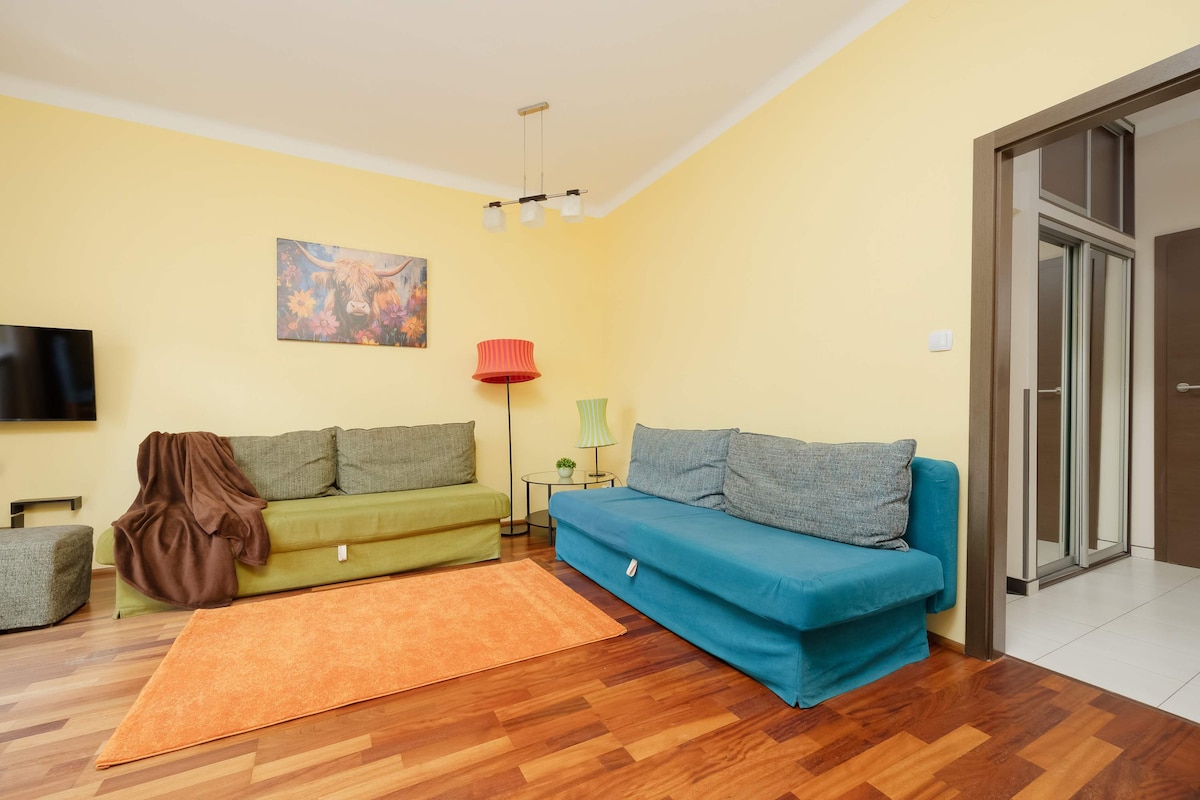 一间舒适的客厅，配有蓝绿色沙发、彩色墙面艺术品和木地板。