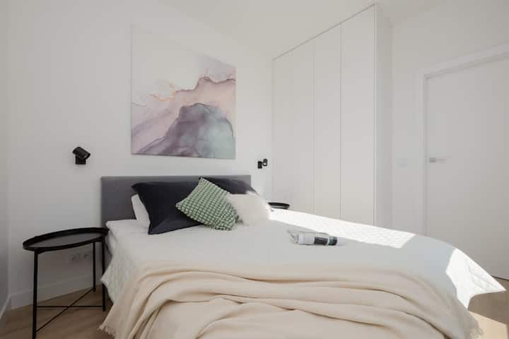 Un dormitorio ordenado con una colcha beige, decoración moderna y arte de pared suave.