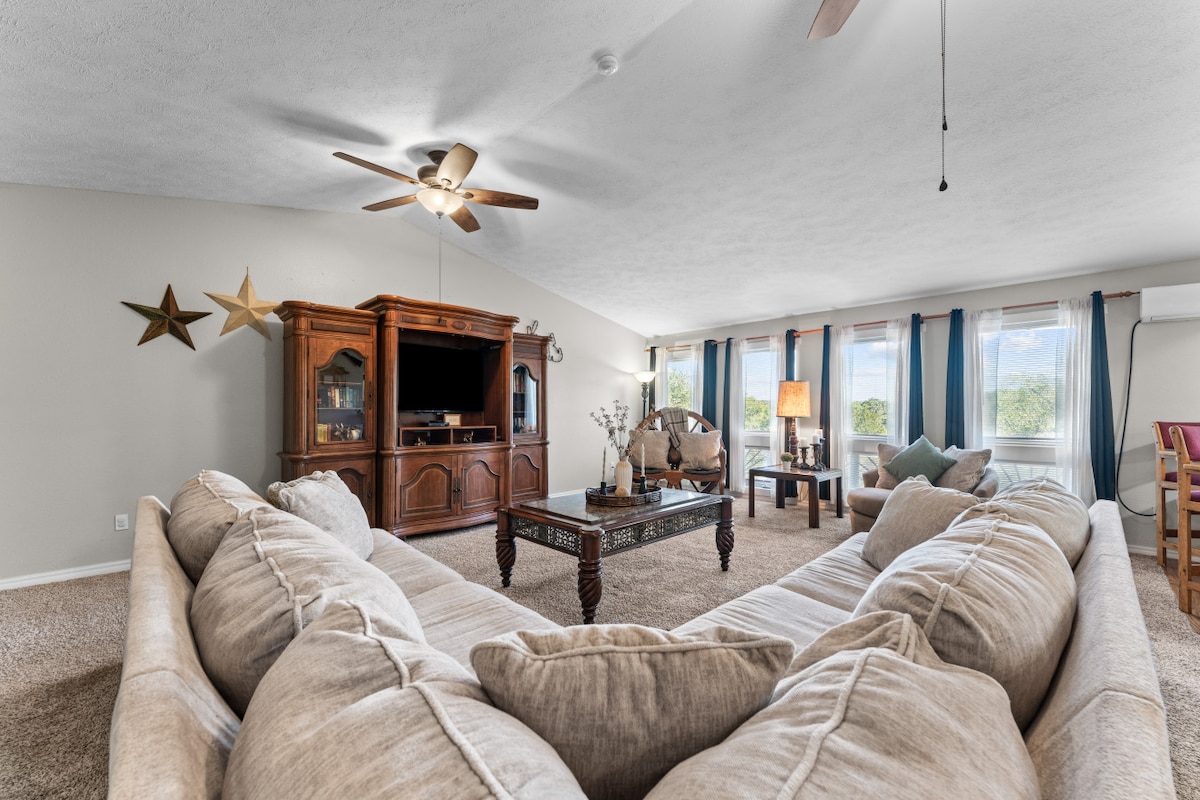 غرفة المعيشة | تصميم واسع مع أريكة قطاعية فاخرة، وإضاءة طبيعية دافئة ولمسات خشبية كلاسيكية