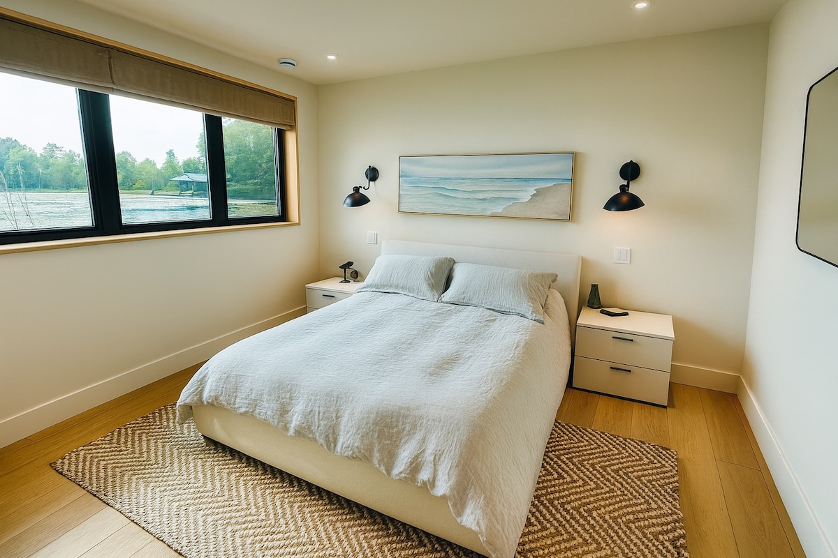 Bright guest room with queen bed and expansive windows overlooking the peaceful bay.