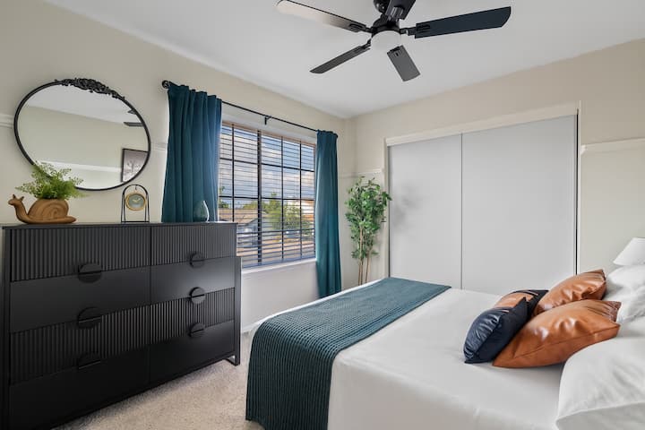 Bedroom 6: A cozy retreat featuring a queen bed styled with warm leather-accent pillows, rich teal accents, and modern black furniture.