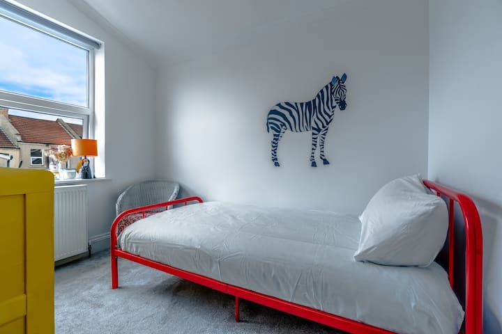 - Camera da letto con letto singolo, telaio rosso e zebra da parete. - La luce della finestra luminosa crea un'atmosfera ariosa e giocosa. - Allestimento confortevole, ideale per bambini o ospiti singoli che soggiornano 