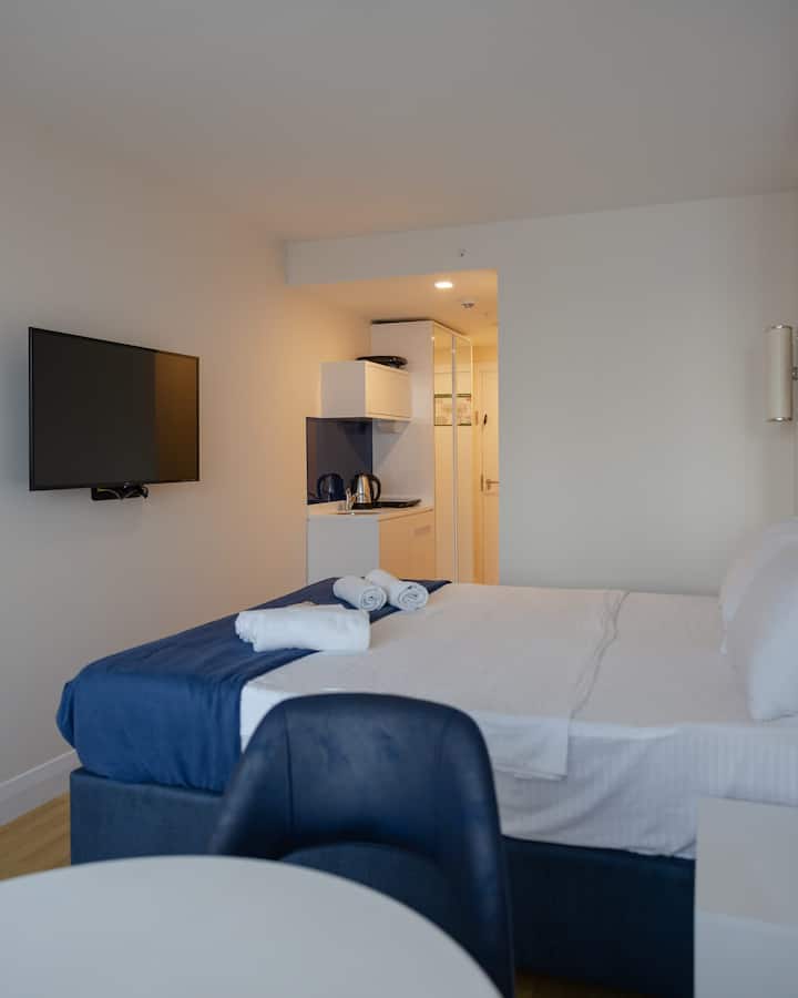 Модерна стая с голямо двойно легло, маса за двама и интелигентно оформление.