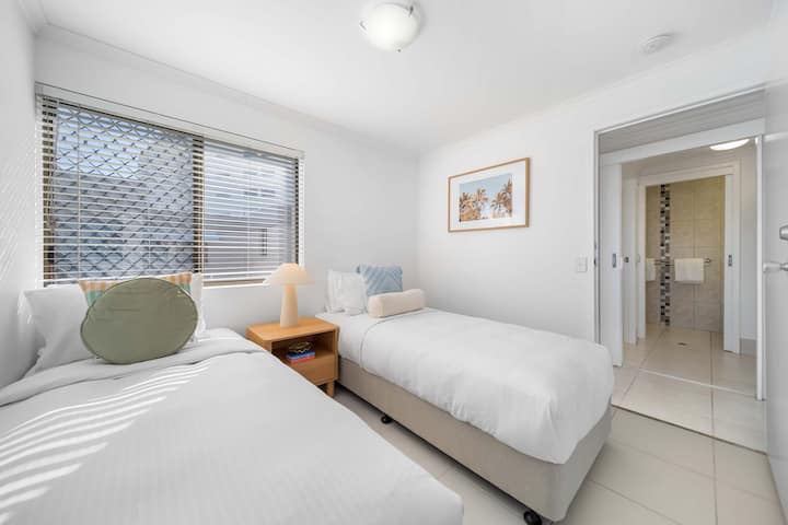 明亮的双人卧室，配有两张单人床和柔软的中性装饰。