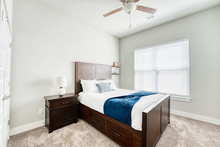  חדר שינה נעים עם מיטת קווין סייז, מצעים נקיים ושמיכה בצבע כחול-ירוק - אידיאלי ללילות מרגיעים.