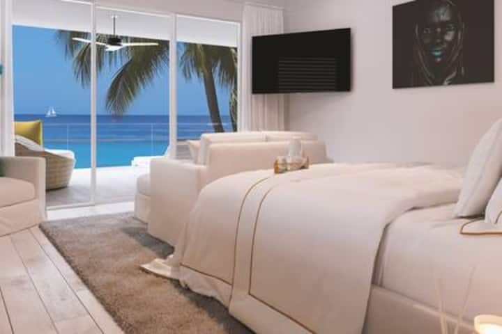 Suite principal impecablemente diseñada en tonos neutros y con impresionantes vistas al mar.  La habitación cuenta con una cama tamaño king, aire acondicionado, ventilador de techo, televisor inteligente, caja fuerte de seguridad, vestidor, sistema de sonido, balcón compartido y baño privado de lujo.