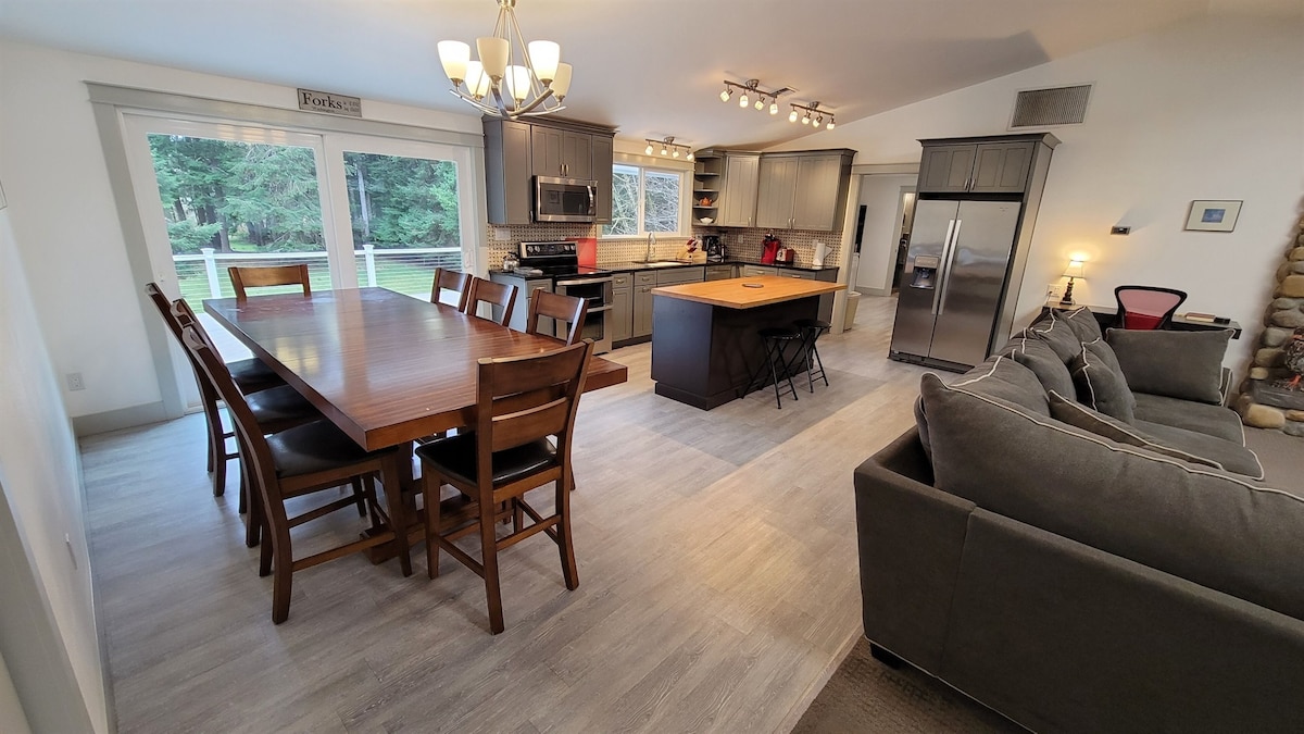 A spacious kitchen and dining area is shown, featuring a large wooden dining table surrounded by eight chairs. Contemporary cabinetry and appliances are visible in the kitchen, along with an island that includes additional seating. A cozy seating arrangement is positioned nearby.