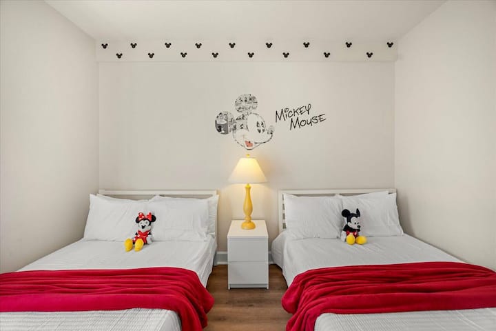 Luminosa y alegre, esta habitación cuenta con dos acogedoras camas adornadas con vibrantes mantas rojas, complementadas con una divertida decoración de Mickey Mouse. Una lámpara encantadora proporciona una luz cálida, creando un ambiente acogedor perfecto para la relajación.