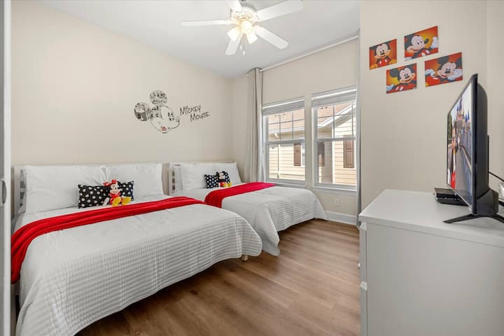 Luminoso y aireado, este alegre dormitorio cuenta con dos acogedoras camas adornadas con sábanas blancas y vibrantes detalles en rojo. La luz natural entra a través de los grandes ventanales, creando un ambiente acogedor perfecto para la relajación.