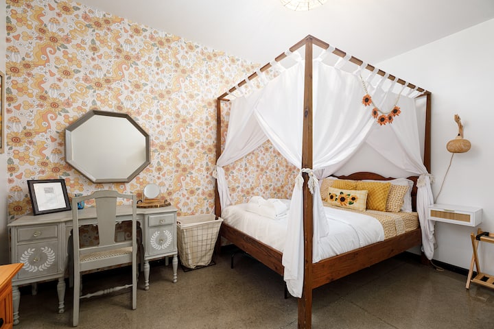 Шармантна спална соба со кревет со балдахин, винтиџ тоалетна масичка и разиграна тапета со цвеќиња за пријатно одморање.