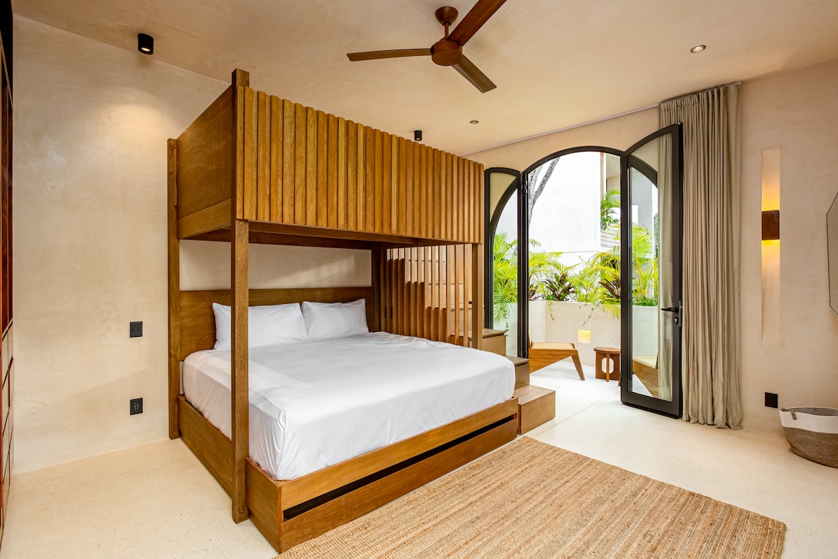 تحتوي غرفة النوم الثالثة الواسعة على سرير خشبي مخصص، وألوان محايدة دافئة، وإمكانية الوصول المباشر إلى تراس خاص يطل على الحديقة.