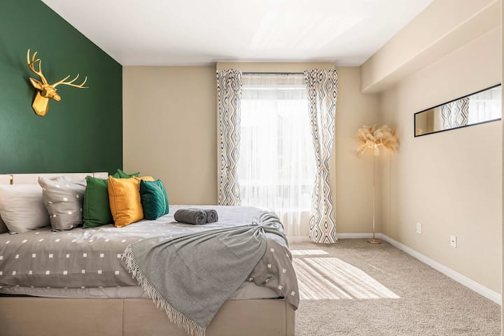 Пространа спална соба со меки беж ѕидови, златни завеси и удобен брачен кревет со мека постелнина.