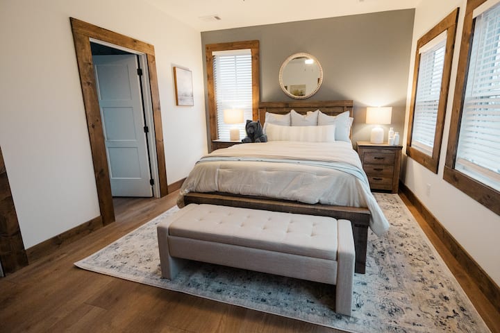 Quarto rústico-chique ensolarado com cama queen size macia, banco e pisos de madeira