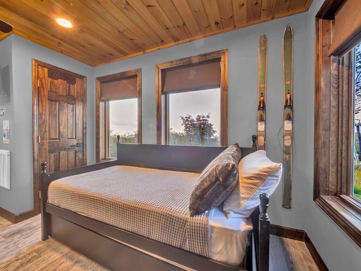 Udobna spavaća soba s pogledom na planine s rustikalnim drvenim detaljima i starinskim skijama koje unose dašak alpskog šarma.