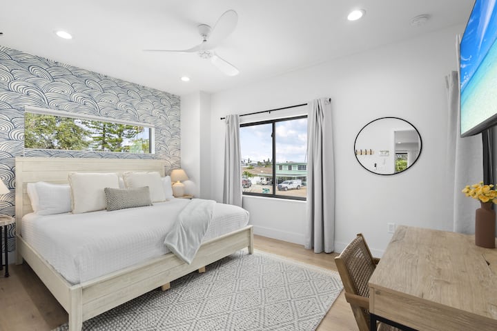 Chumba cha kulala cha mfalme mkali chenye mandhari ya kuvutia, eneo la dawati, na TV iliyowekwa kwa ajili ya mapumziko ya mwisho.