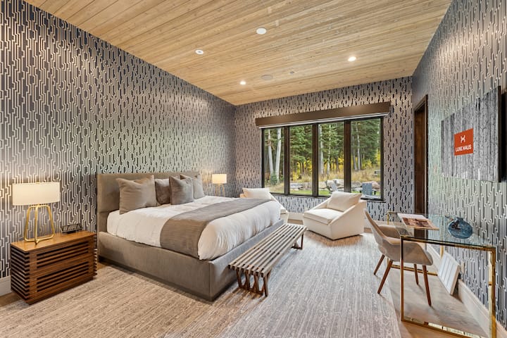 Guest suite with patterned accent wall, vaulted wood ceiling, and forest views