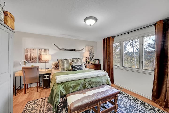 Pokojná hlavná spálňa s útulnou posteľnou bielizňou, malebným výhľadom na les a teplou horskou výzdobou.