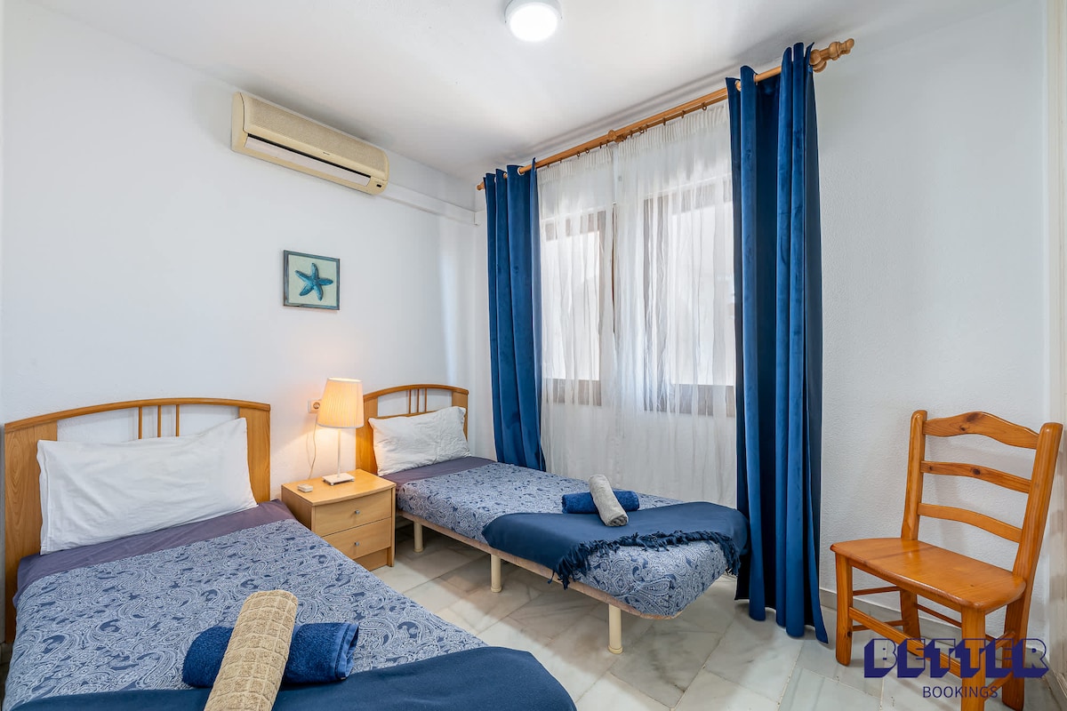 חדר שינה עם שתי מיטות יחיד, וילונות כחולים וכיסא עץ. חדר שינה נעים ומזמין