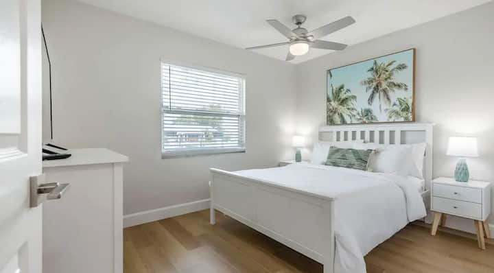 海岸风格的卧室配有舒适的白色床、热带艺术品和柔和的自然光。 宁静的色调和现代风格营造出一个放松的度假胜地，非常适合在阳光明媚的日子后放松身心。