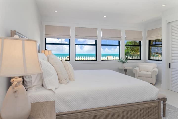 Suite para huéspedes con vistas al mar, tonos relajantes y ropa de cama lujosa.