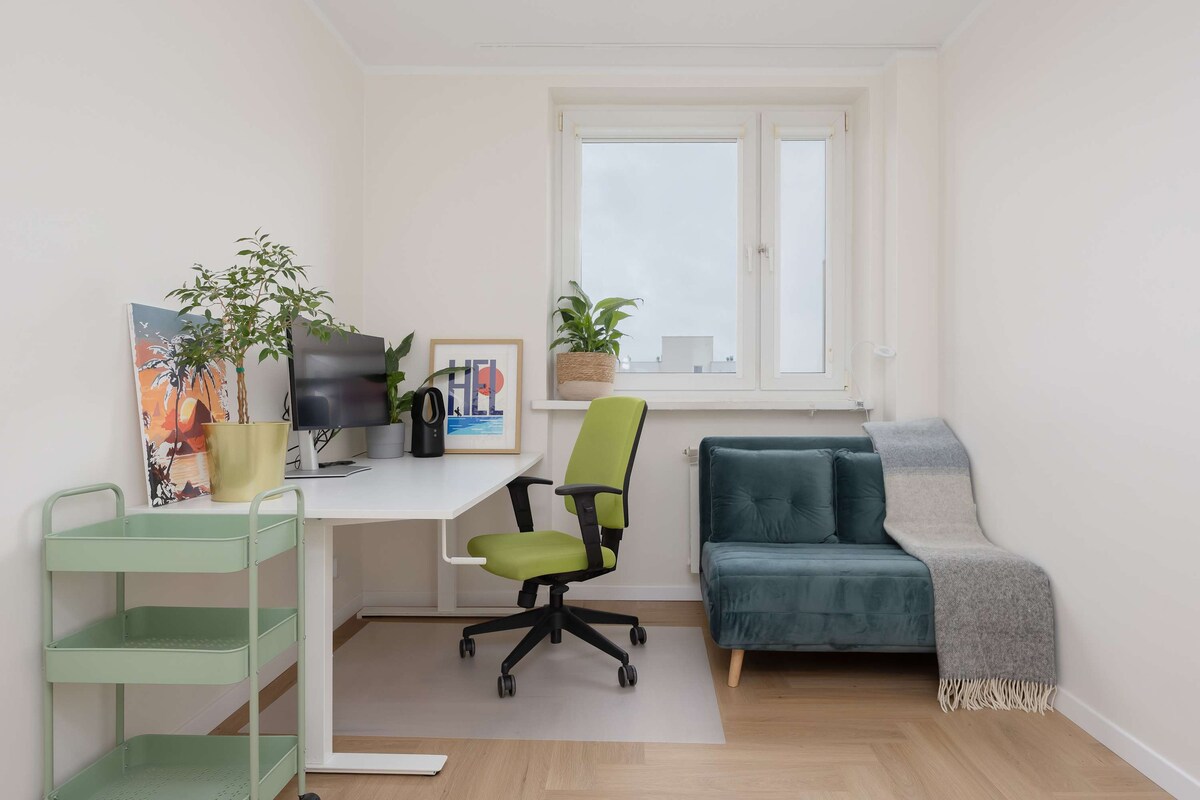 Уютна спалня с разтегателен диван и бюро със стол, гледка и малко зеленина.