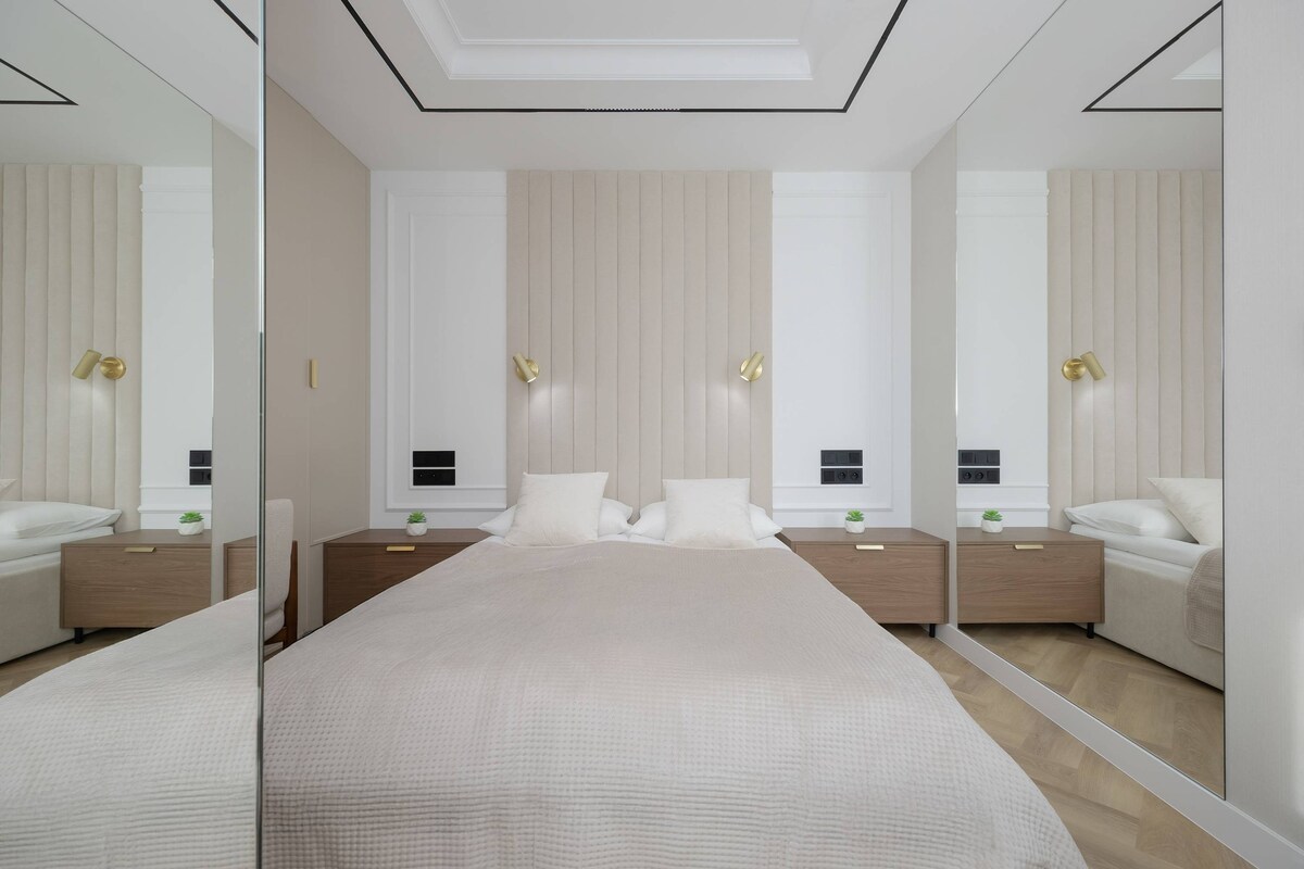 ห้องนอนตกแต่งด้วยโทนสีกลางๆ สร้างความโดดเด่นด้วยความสมมาตรและการตกแต่งแบบกระจกเงาที่เพิ่มความสว่างและความทันสมัยให้กับพื้นที่