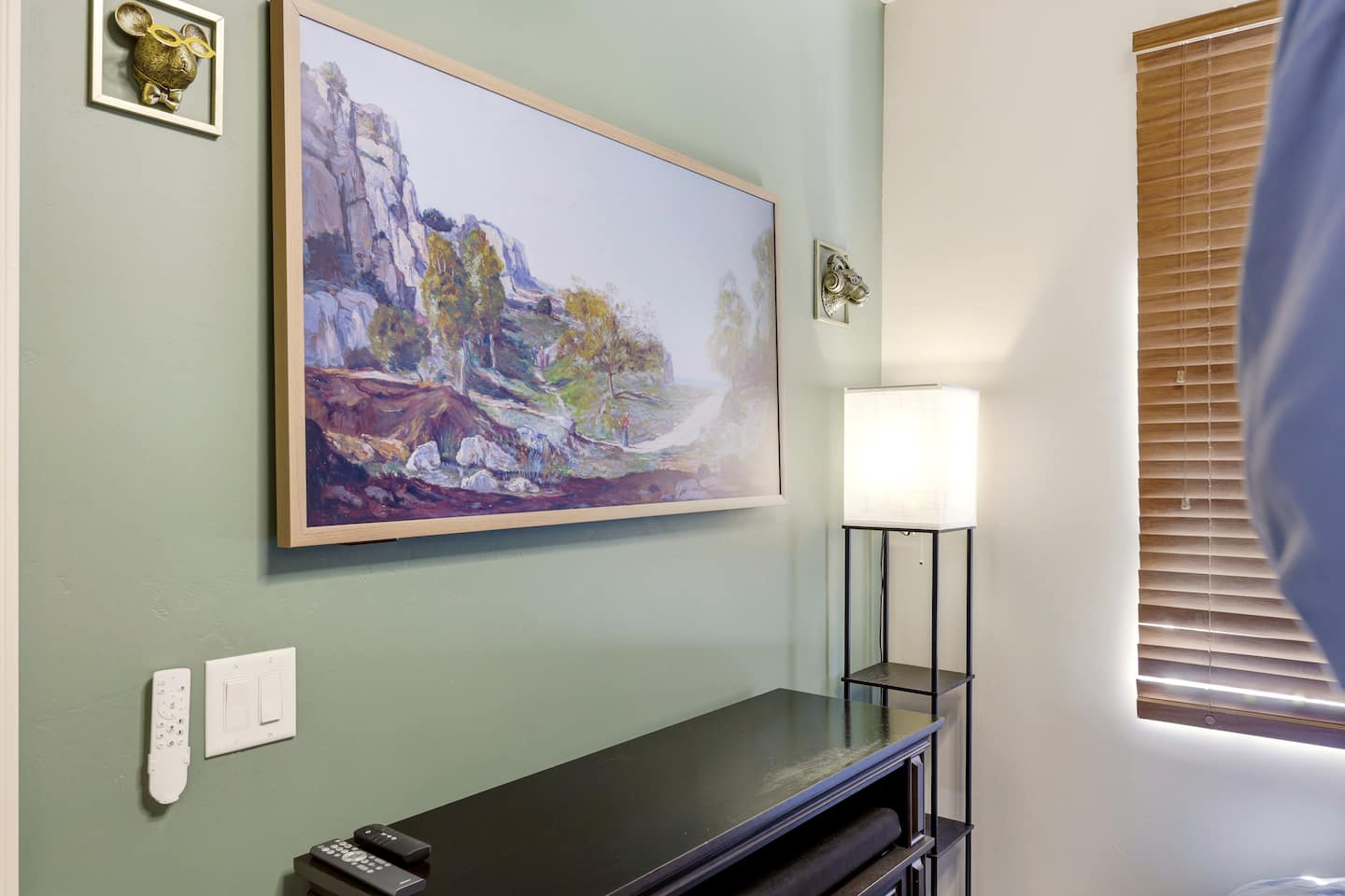 Stylish nook with landscape art, soft lighting, sleek console, and wood blinds