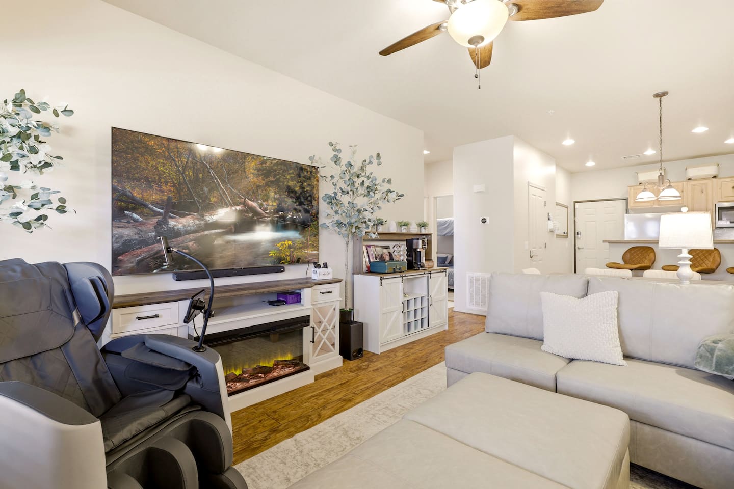 Bright open-plan lounge with big TV, massage chair, and cozy fireplace