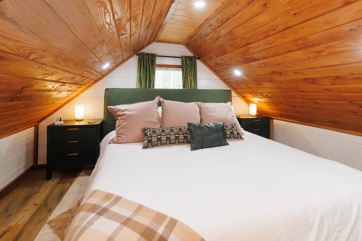 Up in the loft, you’ll find a warm, comfortable bedroom with plush bedding, soft light, and vaulted ceilings that create a peaceful place to unwind.