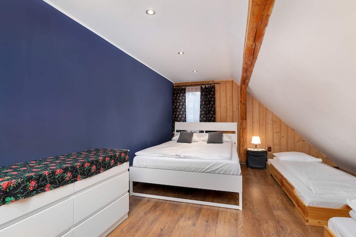 Un dormitorio en el ático con pisos de madera y paredes blancas. Una cama individual y un techo inclinado crean un acogedor rincón para dormir.